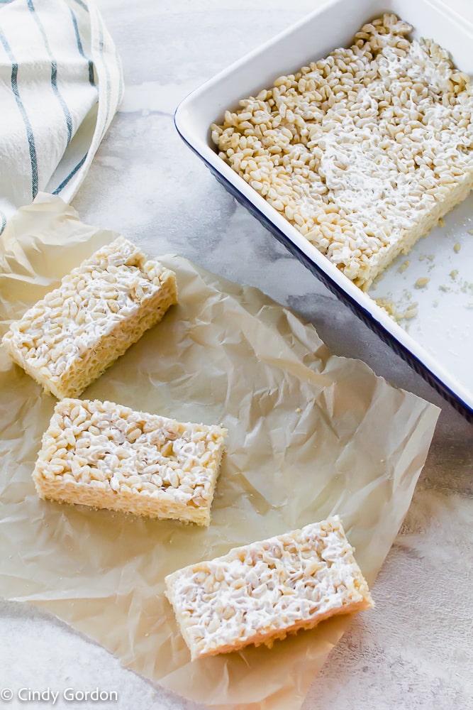 vegan rice krispie treat squares on parchment paper next to a baking dish