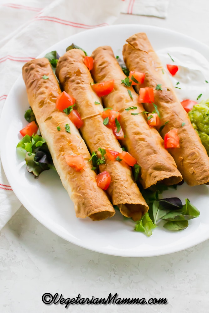 A plate of four vegan taquitos with diced tomatoes