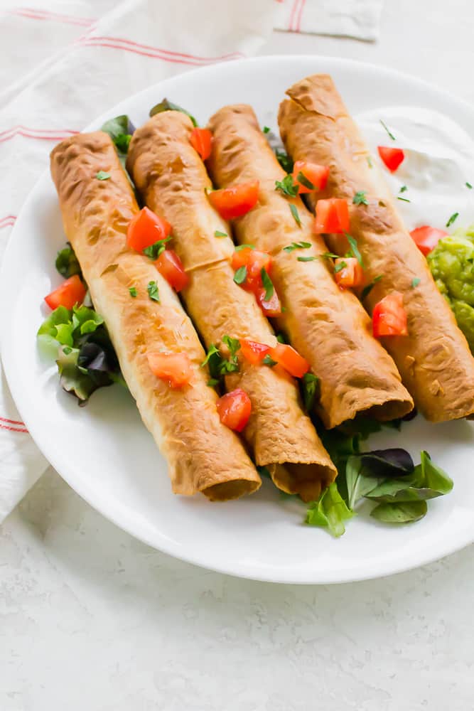 Close-up shot of browned rolled tacos with tomatoes and cilantro on top