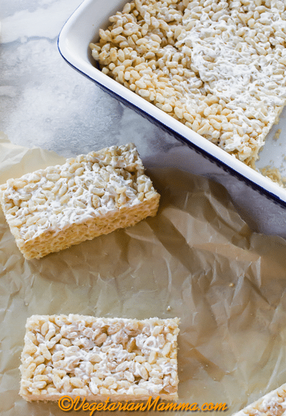 vegan rice krispie treat squares on parchment paper next to a baking dish