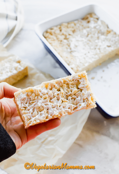 A vegan rice crispy treat in someone's hand above a baking dish