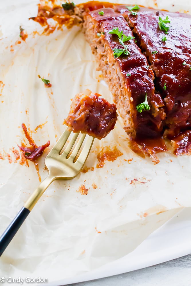 A bite of vegan meatloaf on a fork next to a sliced loaf glazed and garnished with parsley