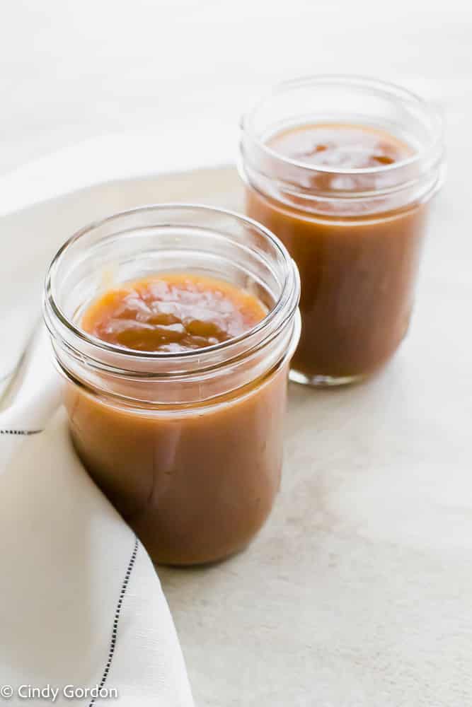Two mason jars of spiced apple butter with a white kitchen towel