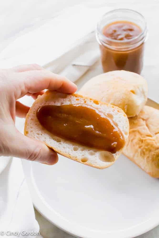 A smear of dairy-free apple butter on crusty bread with loaves and a jar in the background