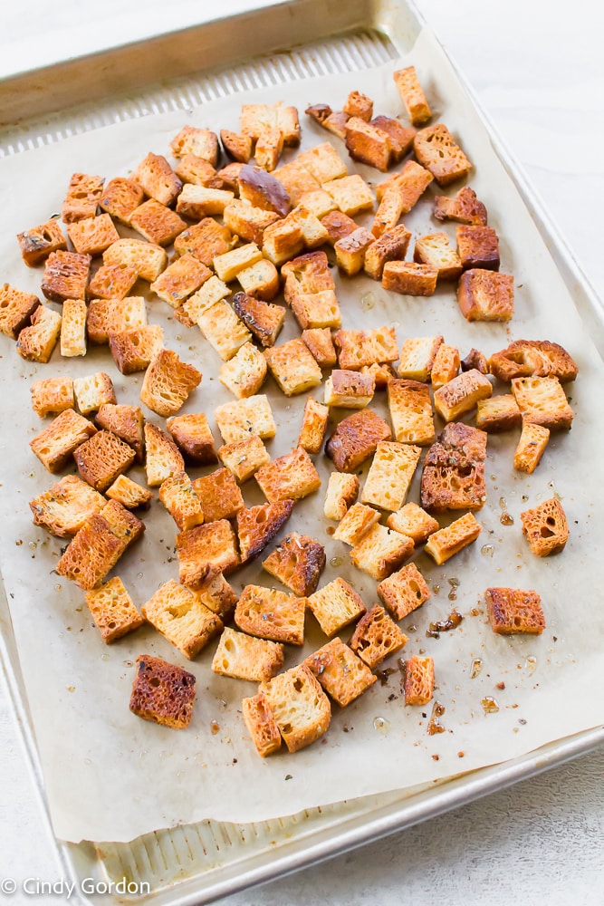 Overhead shot of crunchy vegan croutons baked on parchment paper on a baking sheet 