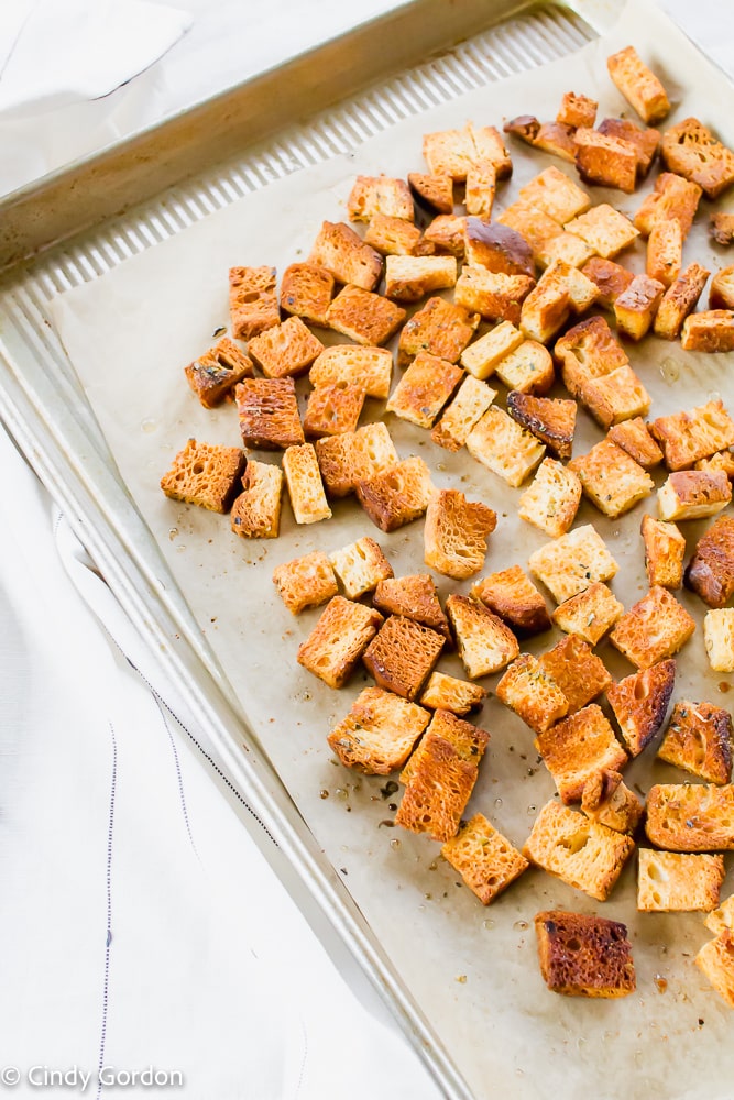 Golden brown homemade croutons on parchment paper in a lipped baking sheet 