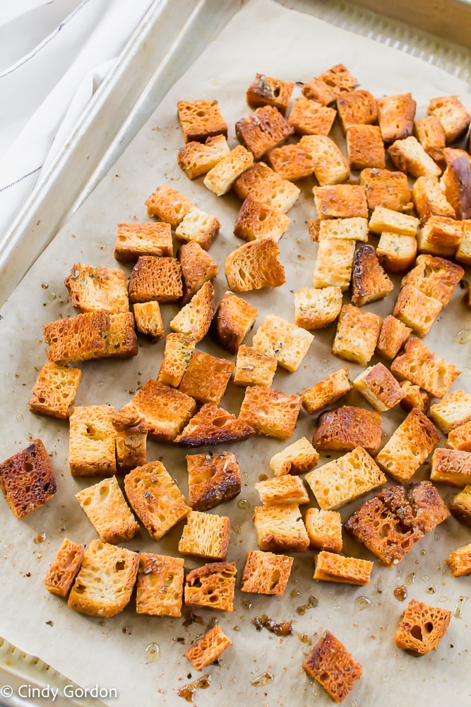 Vegan croutons with oil and Italian seasoning on a baking sheet with parchment paper