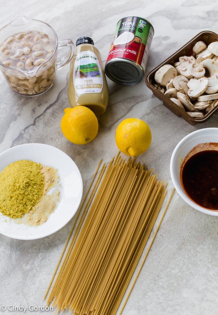 Sliced mushrooms, dry spaghetti, lemons, Dijon mustard, a can of coconut milk, soaking raw cashews and a plate of seasonings