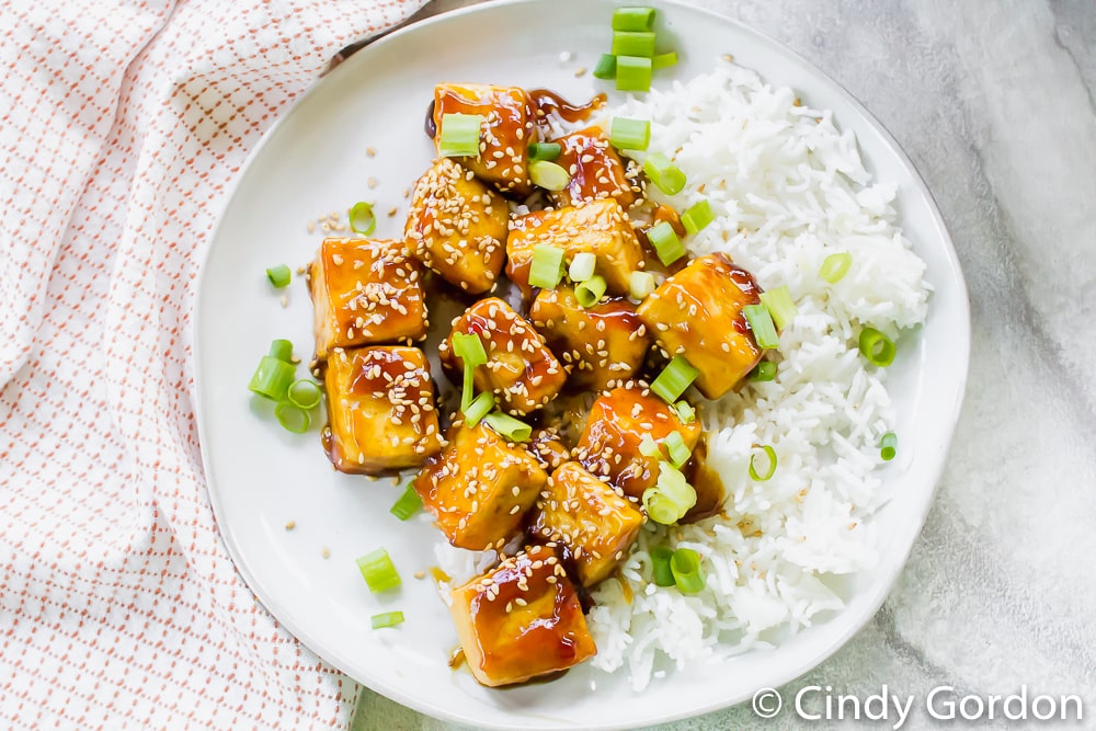 Overhead shot of sauced tofu over white rice with sesame seeds and green onions on top