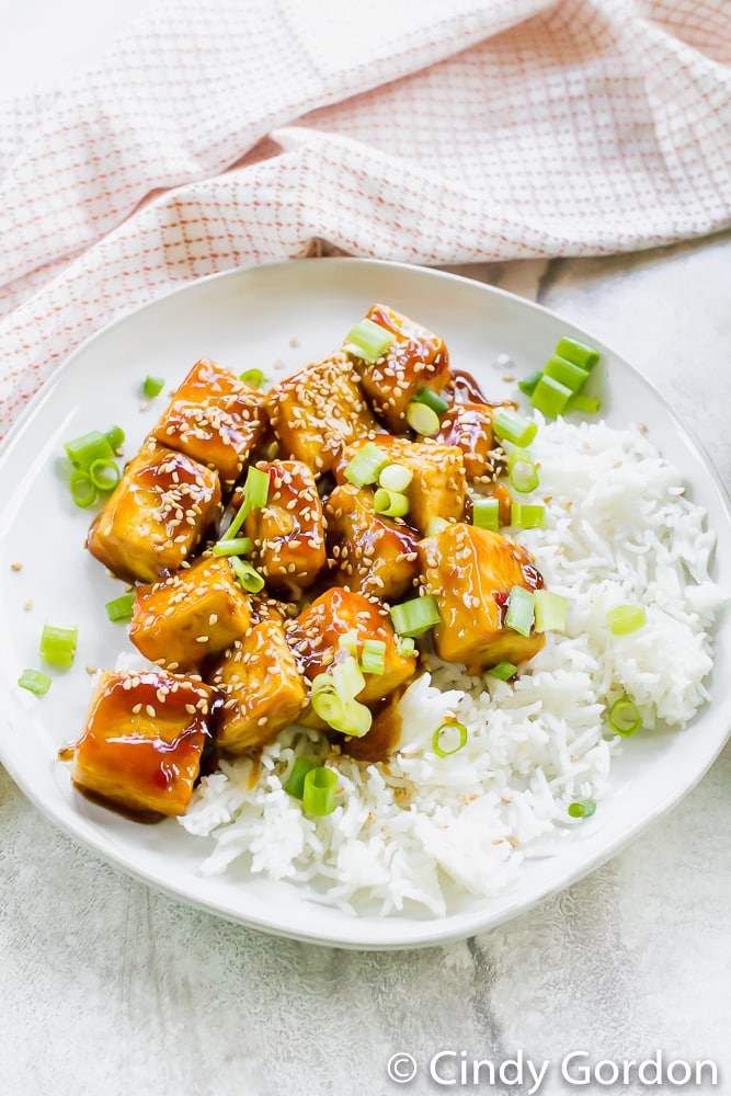 Crispy tofu covered in a honey soy sauce over white rice with green onions and sesame seeds