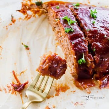 sliced meatloaf on parchment paper, made from beyond meat. a fork is holding a bite.