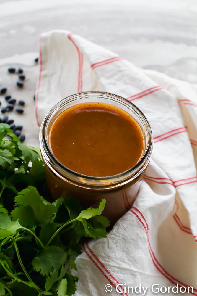 Overhead shot of enchilada sauce in a glass gar with a towel and a bunch of cilantro