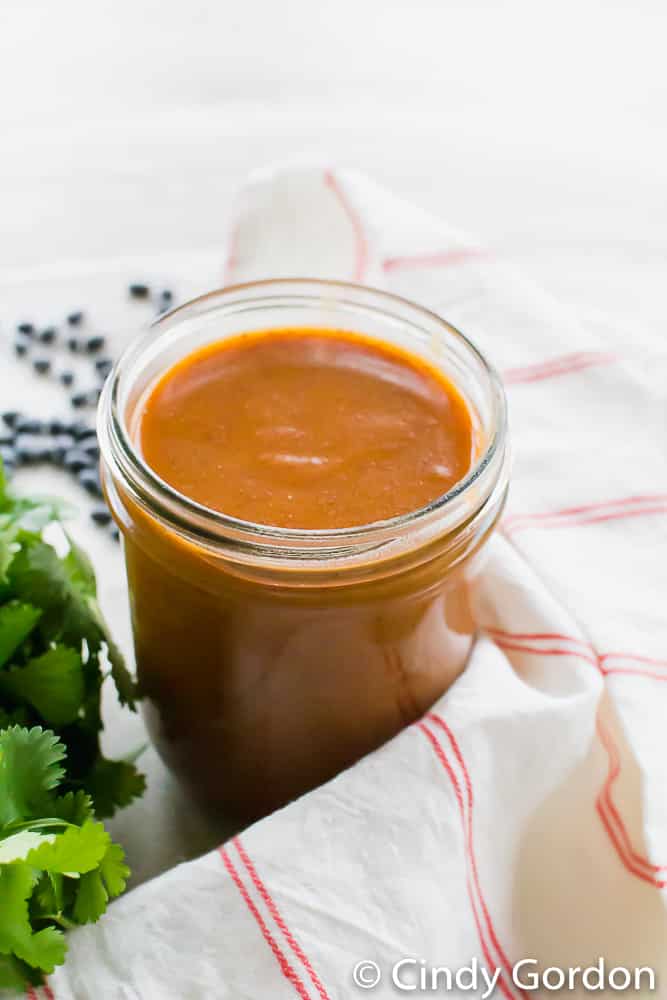 A mason jar of red enchilada sauce with cilantro and a red and white kitchen towel