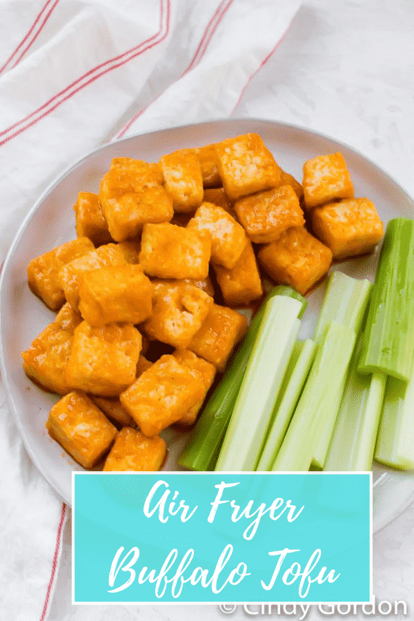 Close-up shot of cubed tofu with buffalo sauce next to celery sticks on a round plate