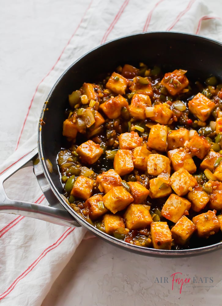 Fried tofu cubes in a deep brown sauce with sautéed onions and peppers in a skillet