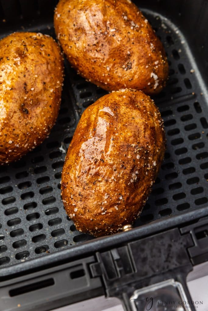three oiled shiny brown potatoes in black air fryer bakset