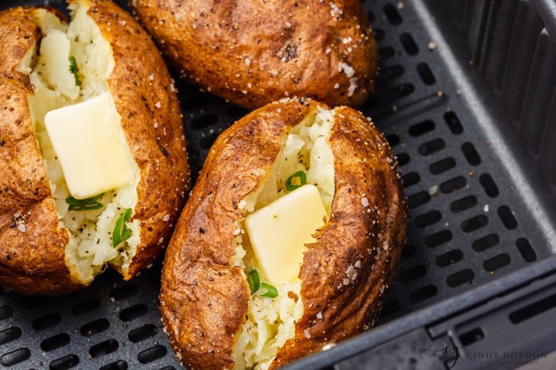 Potatoes have sourcream and parsley, the three potatoes are in a black air fryer basket