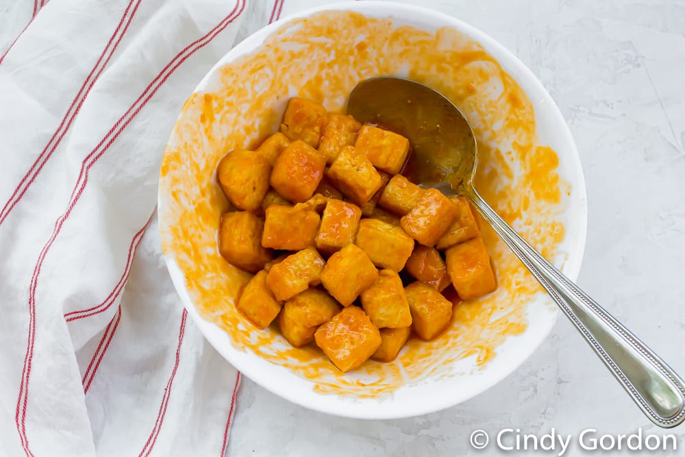 Buffalo sauce tossed with tofu in a bowl.