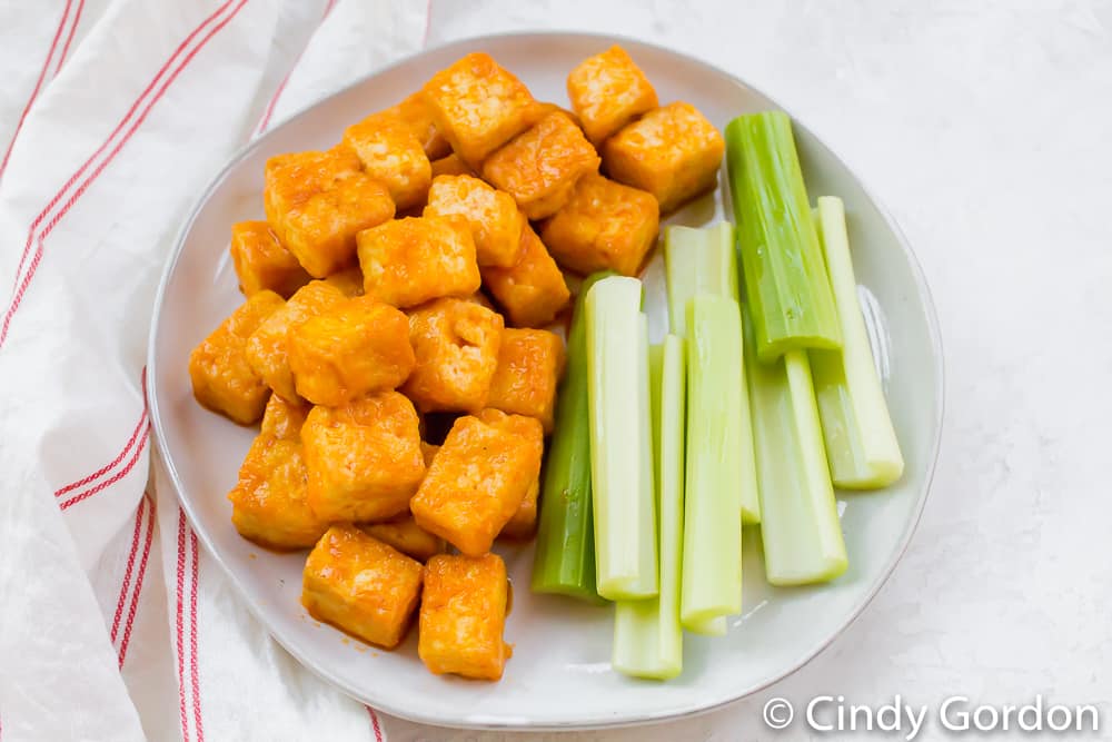 A white plate of celery sticks and buffalo tofu cubes