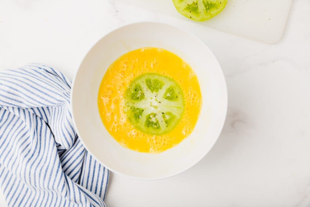 white bowl with whisked egg and green tomato in liquid