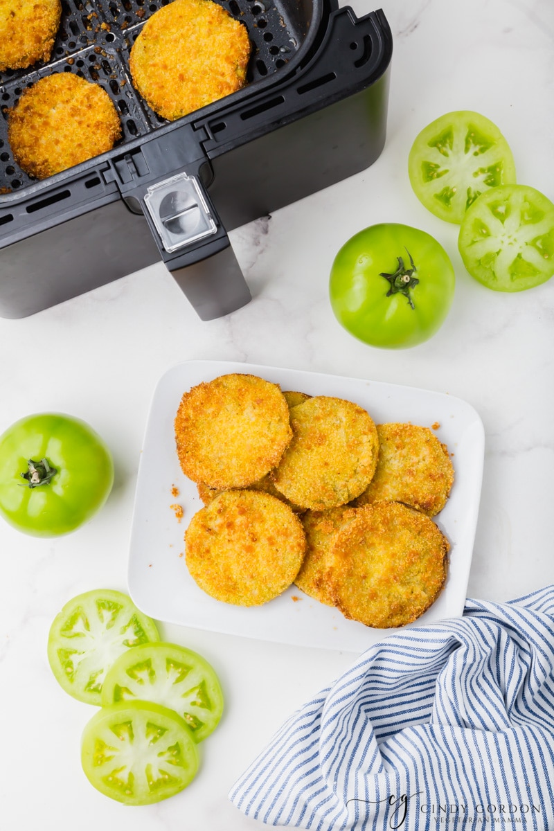 golden brown bread air fryer fried green tomatoes on a white plate with black air fryer basket in background