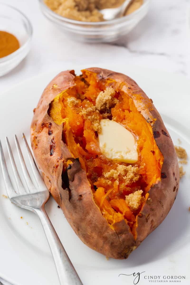 one air fryer baked sweet potatoes cut open with a square of butter and cinnamon on top. placed on a plate