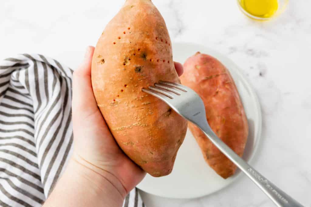 hand holding sweet potato and other hand poking it with fork