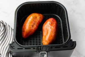 two oiled sweet potatoes in air fryer basket