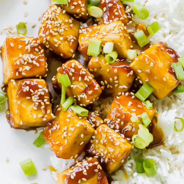 Close up shot of the Sticky, crispy sesame tofu on a white plate with white rice.
