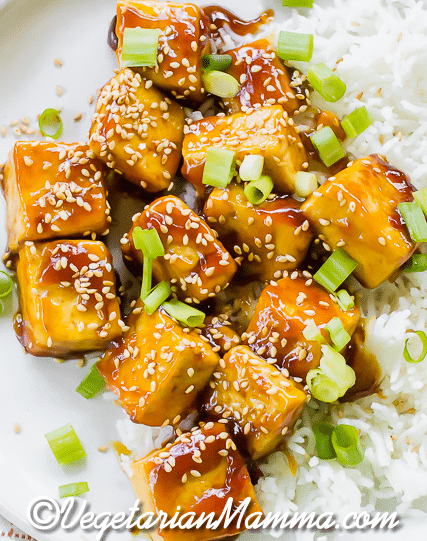 Close up shot of the Sticky, crispy sesame tofu on a white plate with white rice.