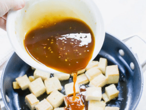 Sticky, sesame sauce poured over the crispy tofu in a pan.