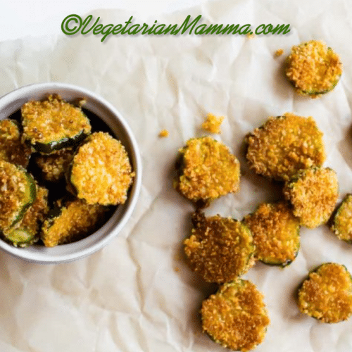 A white bowl of gluten-free fried pickles and a few pickles on parchment paper.