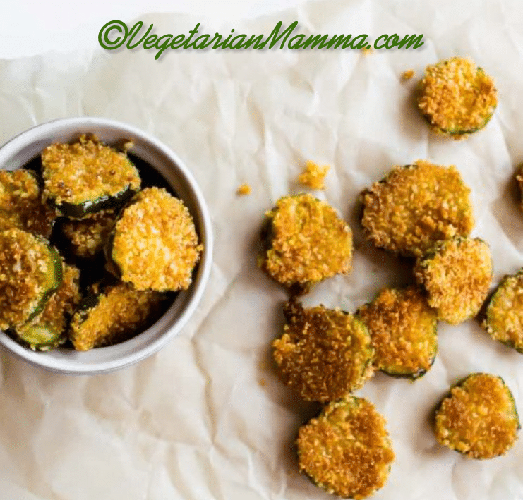 A white bowl of gluten-free fried pickles and a few pickles on parchment paper. 