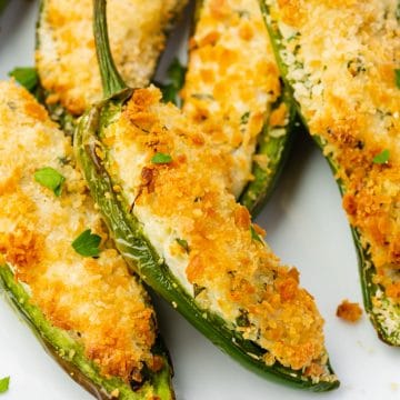 up close shot o white plate full of sliced open jalapeno peppers that are stuffed with white and green cream cheese and golden brown breading.