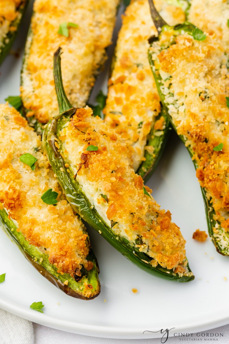 up close shot o white plate full of sliced open jalapeno peppers that are stuffed with white and green cream cheese and golden brown breading. 