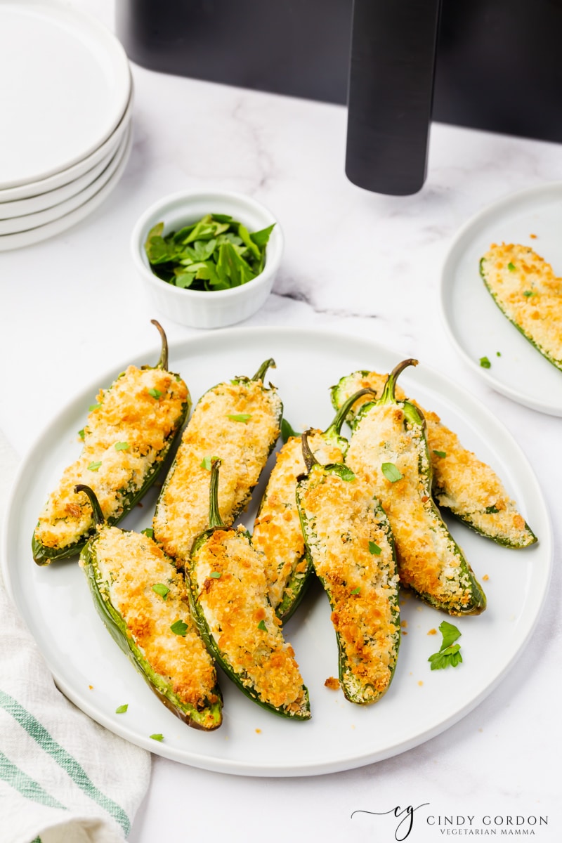 white plate full of sliced open jalapeno peppers that are stuffed with white and green cream cheese and golden brown breading.