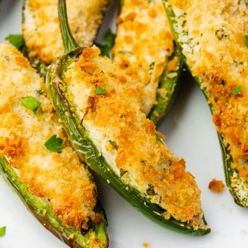 white plate full of sliced open jalapeno peppers that are stuffed with white and green cream cheese and golden brown breading.