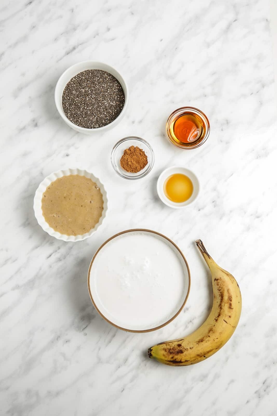 Bowls of chia seeds, maple syrup, coconut milk, vanilla syrup, cinnamon,  and mashed banana with a fresh banana