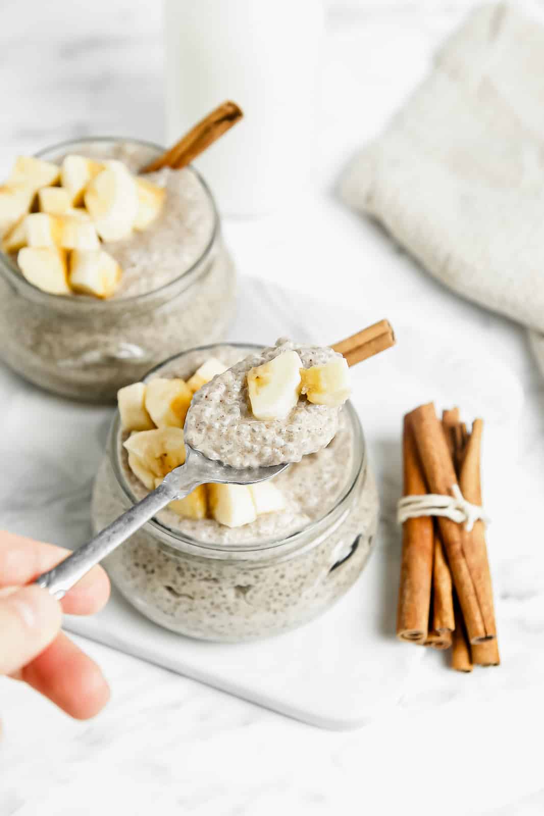 A spoonful of banana chia seed pudding over a jar of pudding next to a cinnamon stick bundle