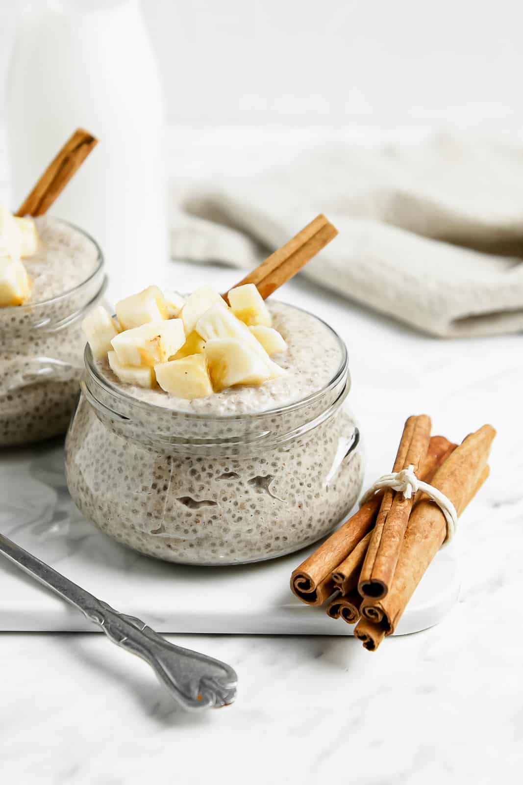 Close-up shot of chia seed pudding in a glass jar topped with banana chunks and a cinnamon stick