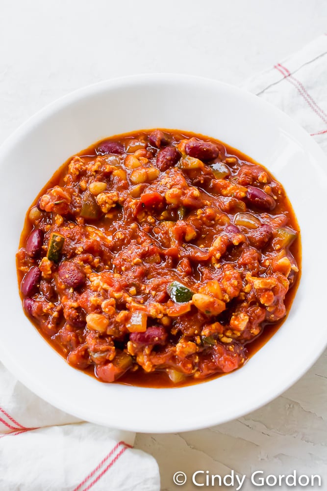 A hearty bowl of vegan chili with beans, zucchini, tomatoes, and tofu in a round white bowl