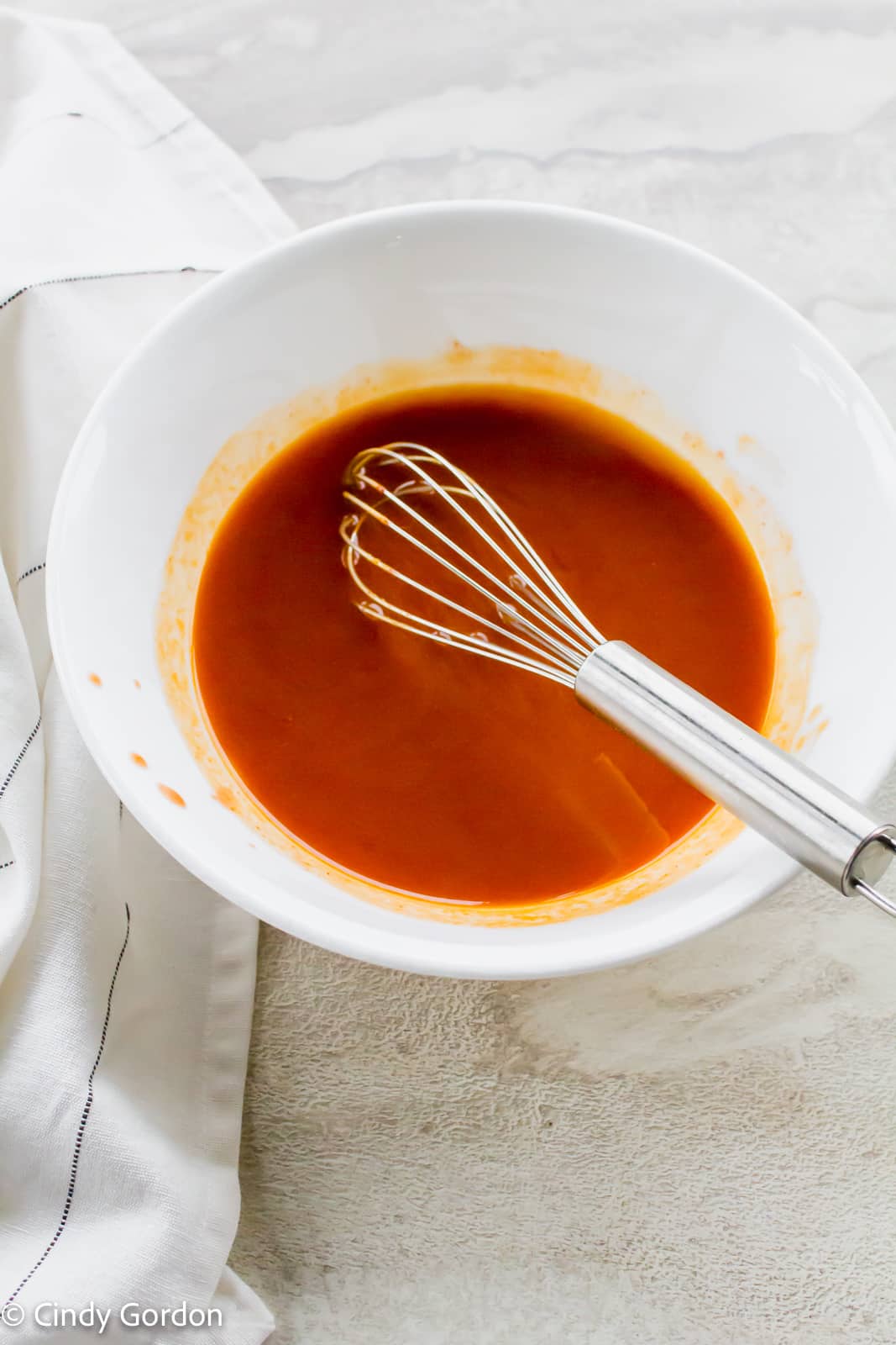 Bright red Buffalo sauce in a large white mixing bowl with a whisk in the bowl