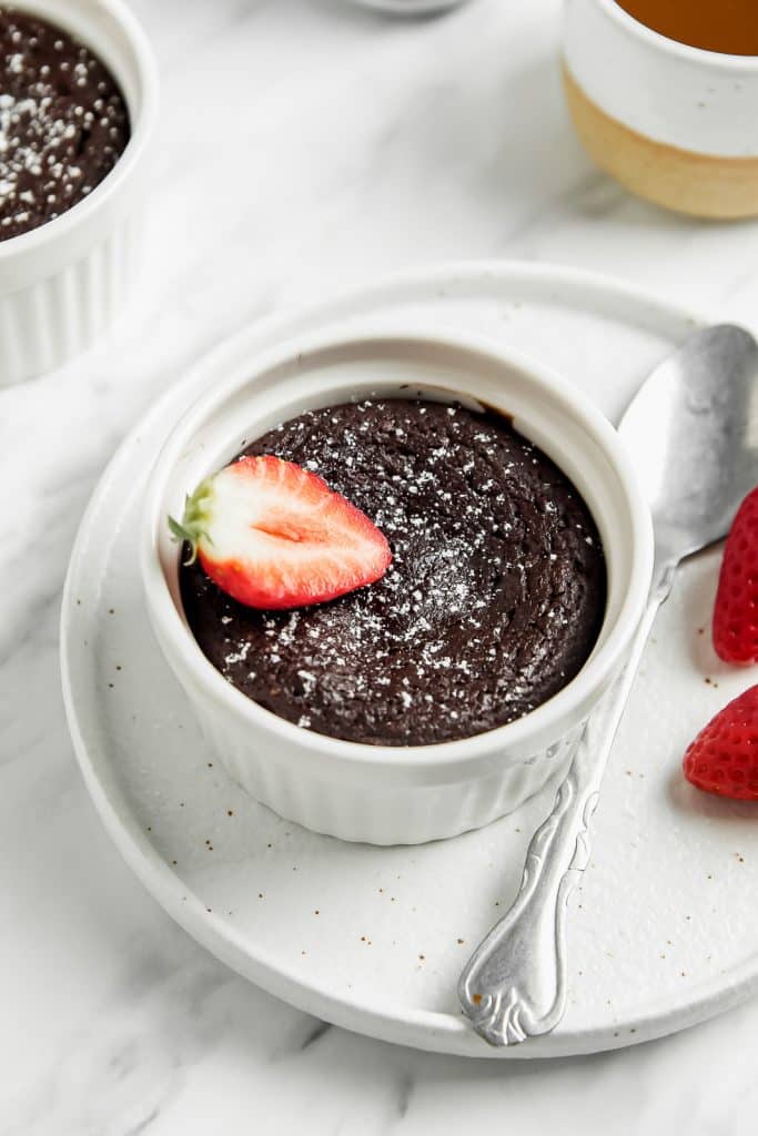 Overhead shot of a chocolate mug cake garnished with powdered sugar and a strawberry slice on a white plate