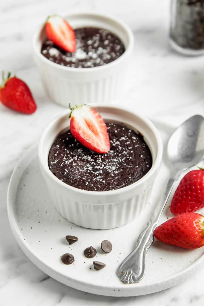 2 chocolate cakes in white ramekins topped with fresh strawberry slices