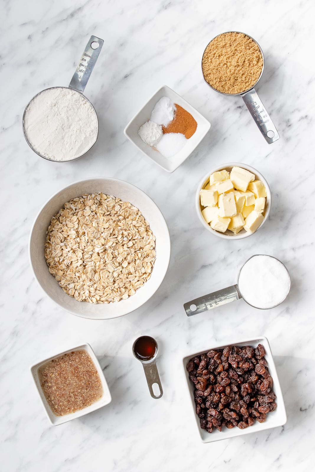 Bowls and measuring cups of brown sugar, caster sugar, gluten-free flour, butter, oats, and raisins