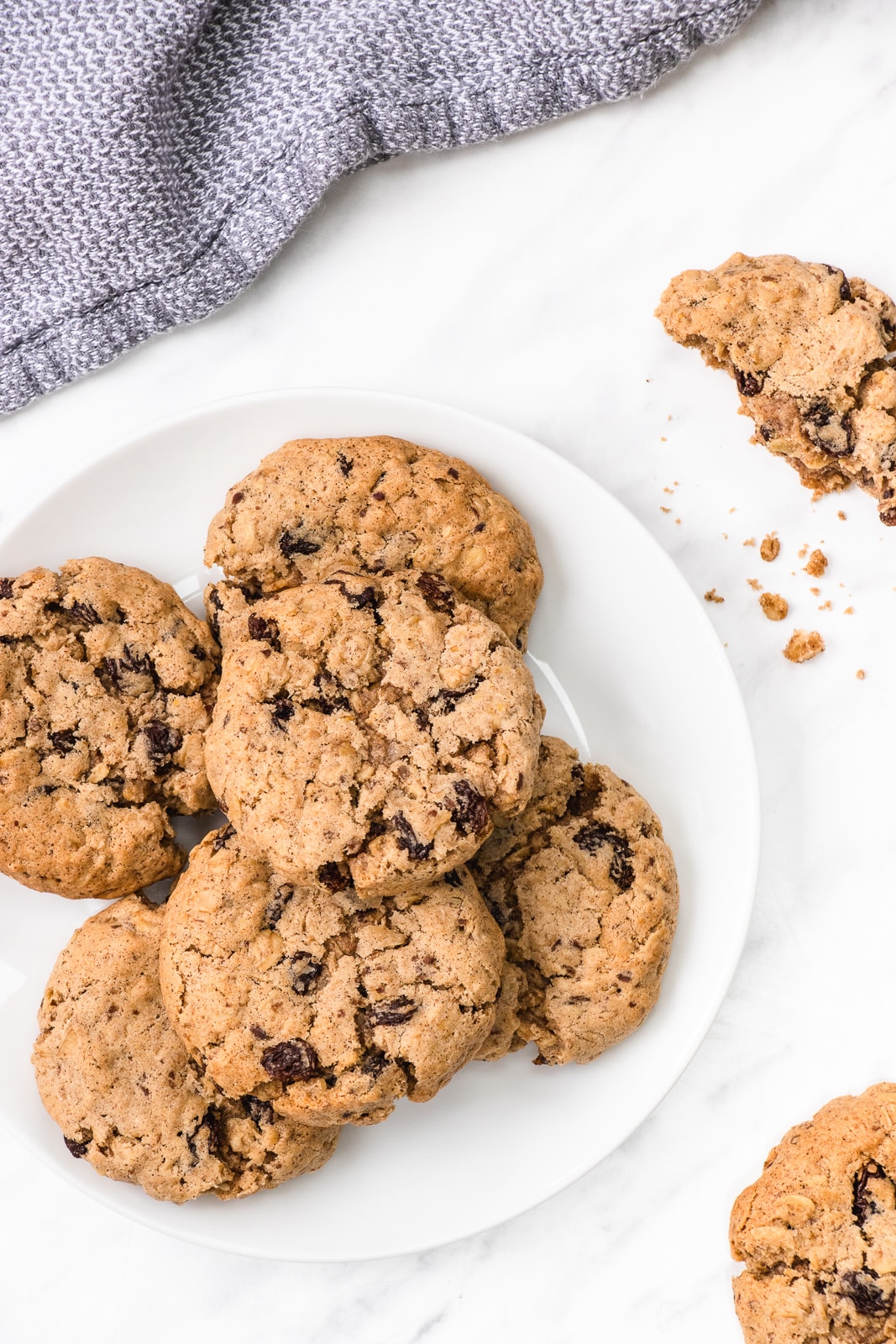 A stack of oatmeal raisin cookies on a round white plate surrounded by more cookies and some crumbs