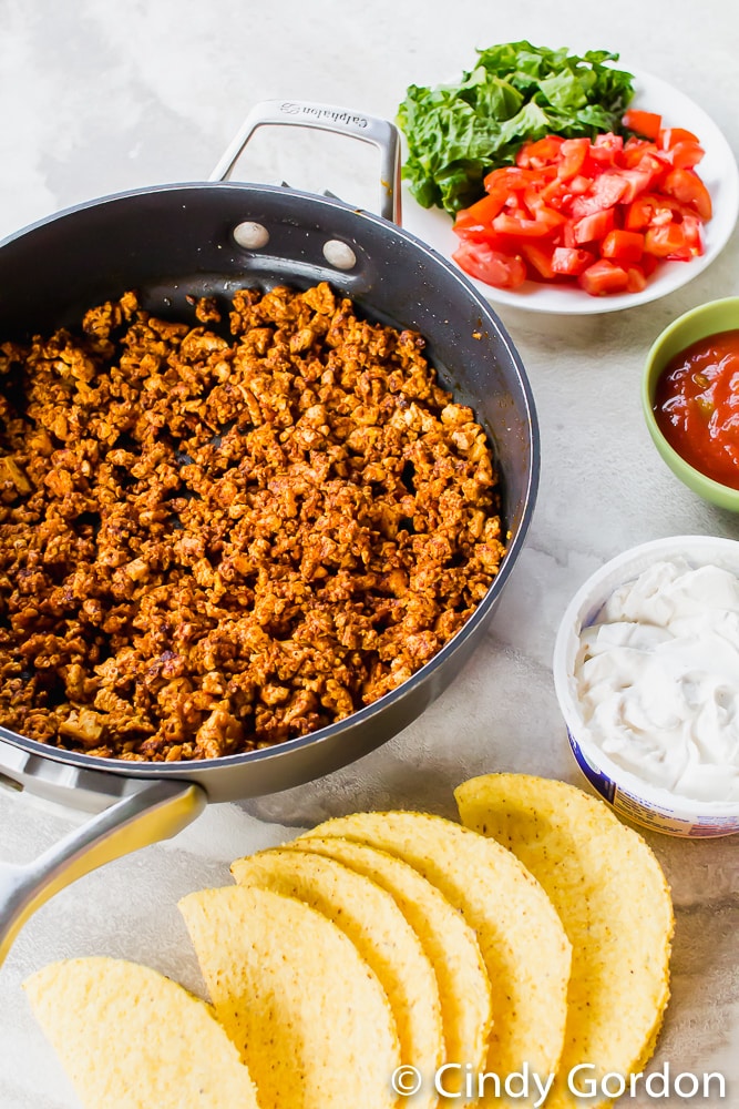 Close-up shot of seasoned tofu, hard taco shells, salsa, sour cream, and vegetables