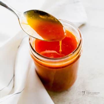 a small jar of vegan buffalo sauce, a spoon is lifting some up.
