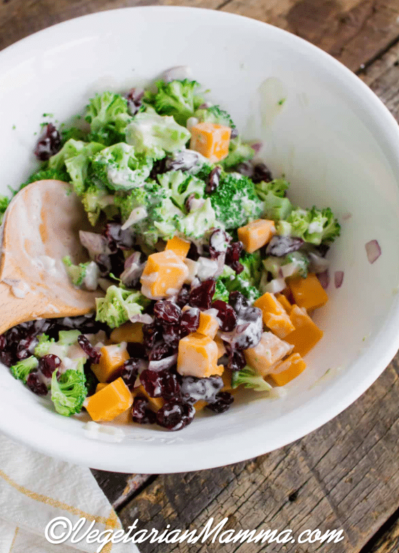 Spoon inside bowl of broccoli salad atop wooden pallet