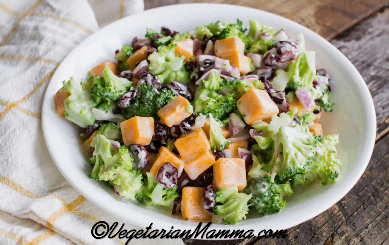 broccoli, cheddar cheese cubes, and cranberries in a creamy dressing in a white bowl.